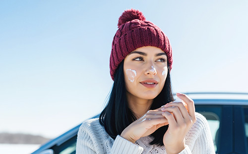 young adult woman rubbing sunscreen on to her face in the Winter to help prevent skin cancer